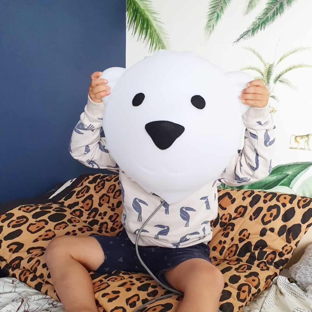 Criança sentada na cama a segurar à frente da sua cara a lâmpada Bjorn Medium - Uma Luz interior LED em forma de urso polar da marca Flow Amsterdam