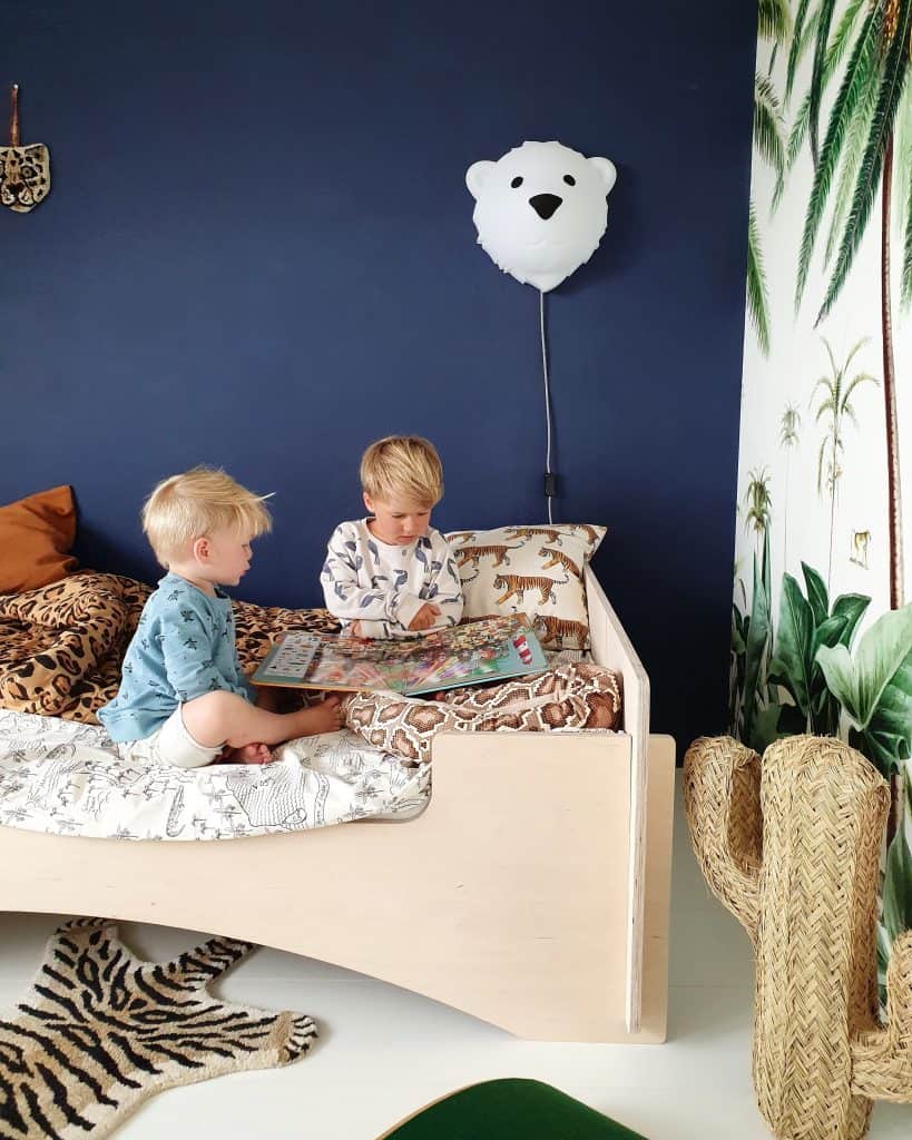 Duas crianças sentadas numa cama, com a lâmpada Bjorn fixada na parede. A lâmpada Bjorn Medium é uma Luz interior LED em forma de urso polar da marca Flow Amsterdam