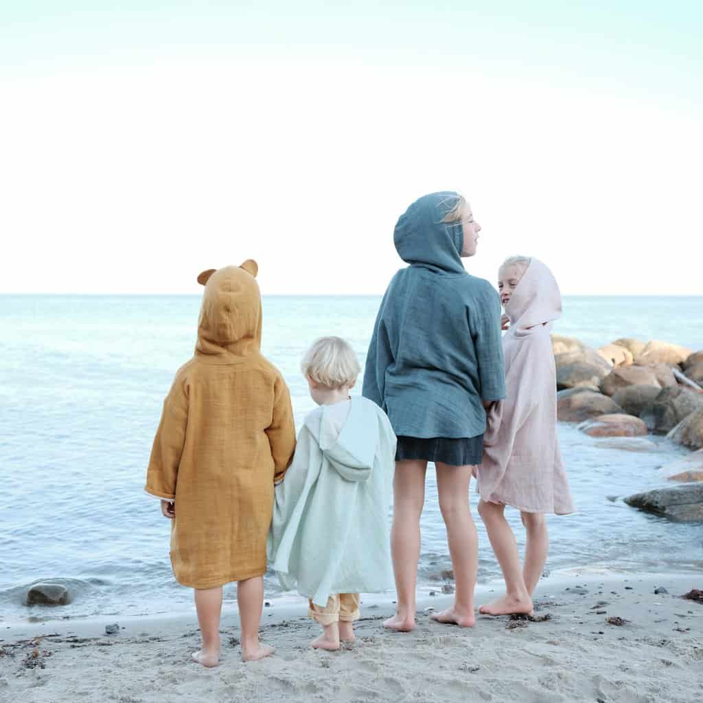 Quatro crianças na praia vestidas com Roupão com capuz e toalhas-poncho da marca Fabelab