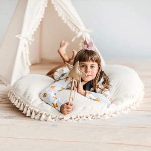 Criança deitada numa Almofada grande para o chão decorada com borlas