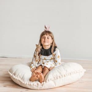 Criança sentada na Almofada grande para o chão decorada com pompons